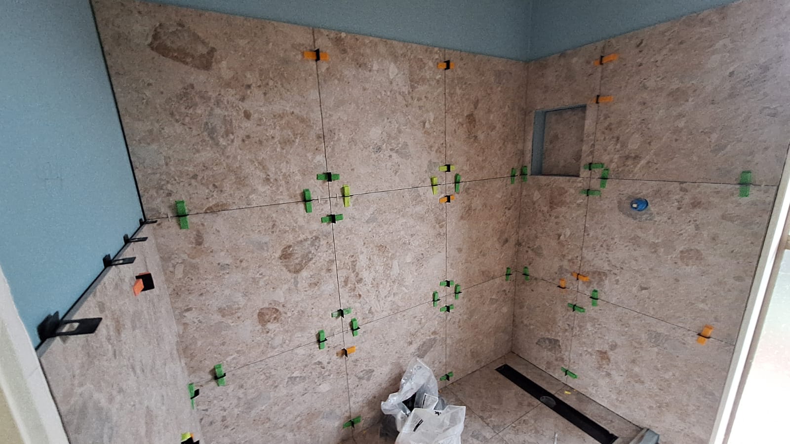 Large-format wall tiles being set with levelling clips during an Auckland tiling job